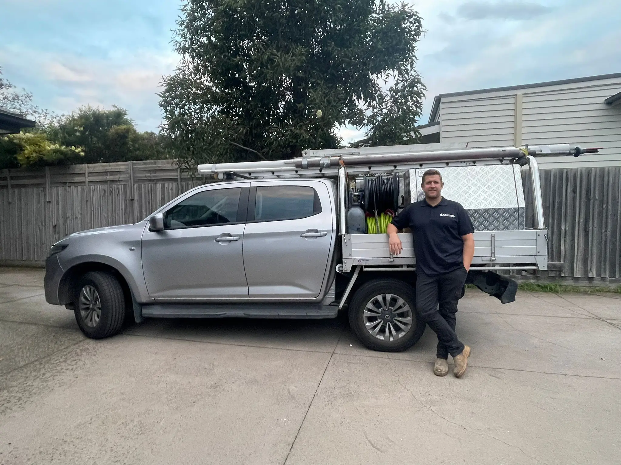 A subcontractor working with AC Plumbing beside the silver dual-cab ute, loaded with hose reels and gear.